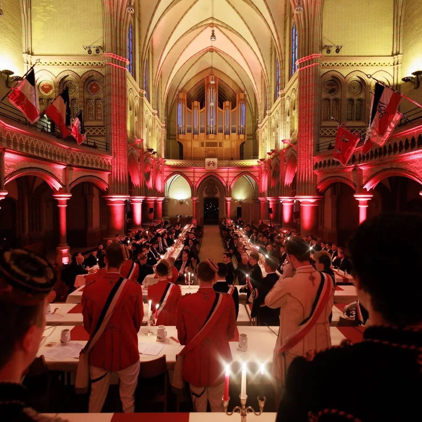 Festkommers in einer Kirche mit Kerzenlicht und rot beleuchtetem Gewölbe